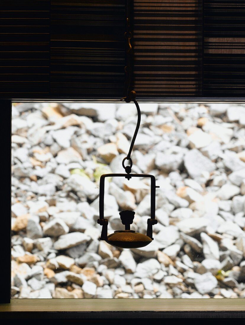 Metal vessel hanging in front of window and view of stones