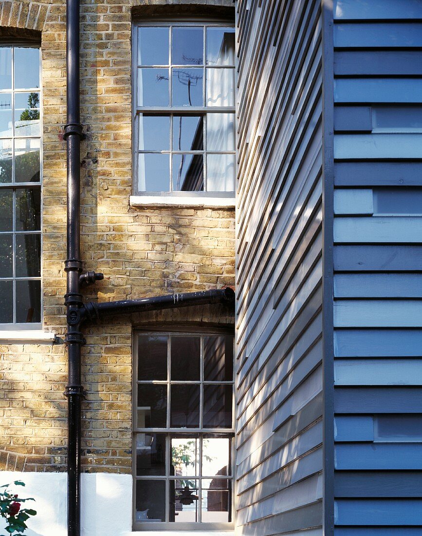 Fassade mit blau gestrichenen Holzlatten vor englischem Wohnhaus mit Ziegelfassade