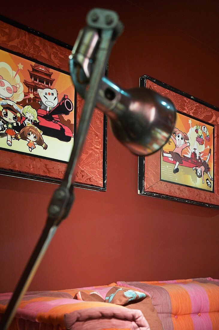 Chrome standard lamp in front of framed cartoons on a red wall