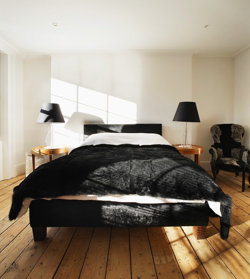 Rahmen eines Doppelbettes und Tagesdecke aus schwarzem Fell im weissen Schlafraum