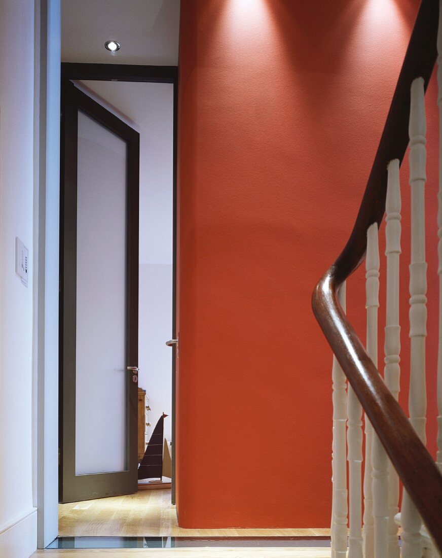 Treppenhaus mit rot getönter Wand neben offener Glastür