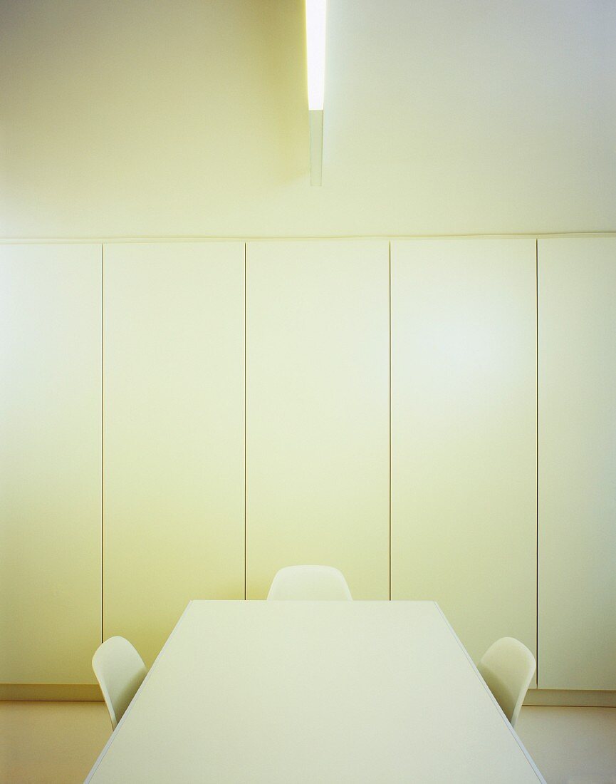 Schlichter Raum mit weißem Tisch und Stühlen vor Einbauschrank