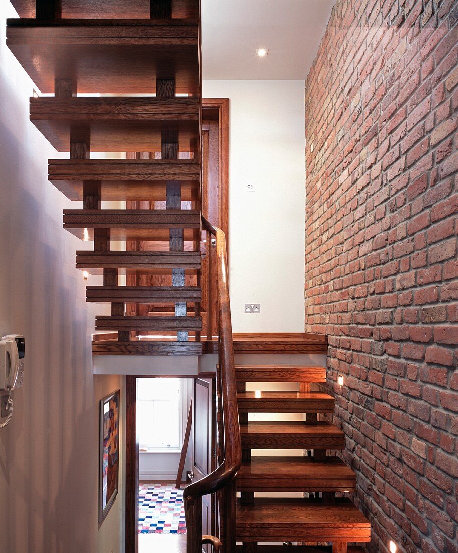 Zweiläufige Holztreppe entlang Sichtziegelwand mit Lichtspots in englischem Wohnhaus