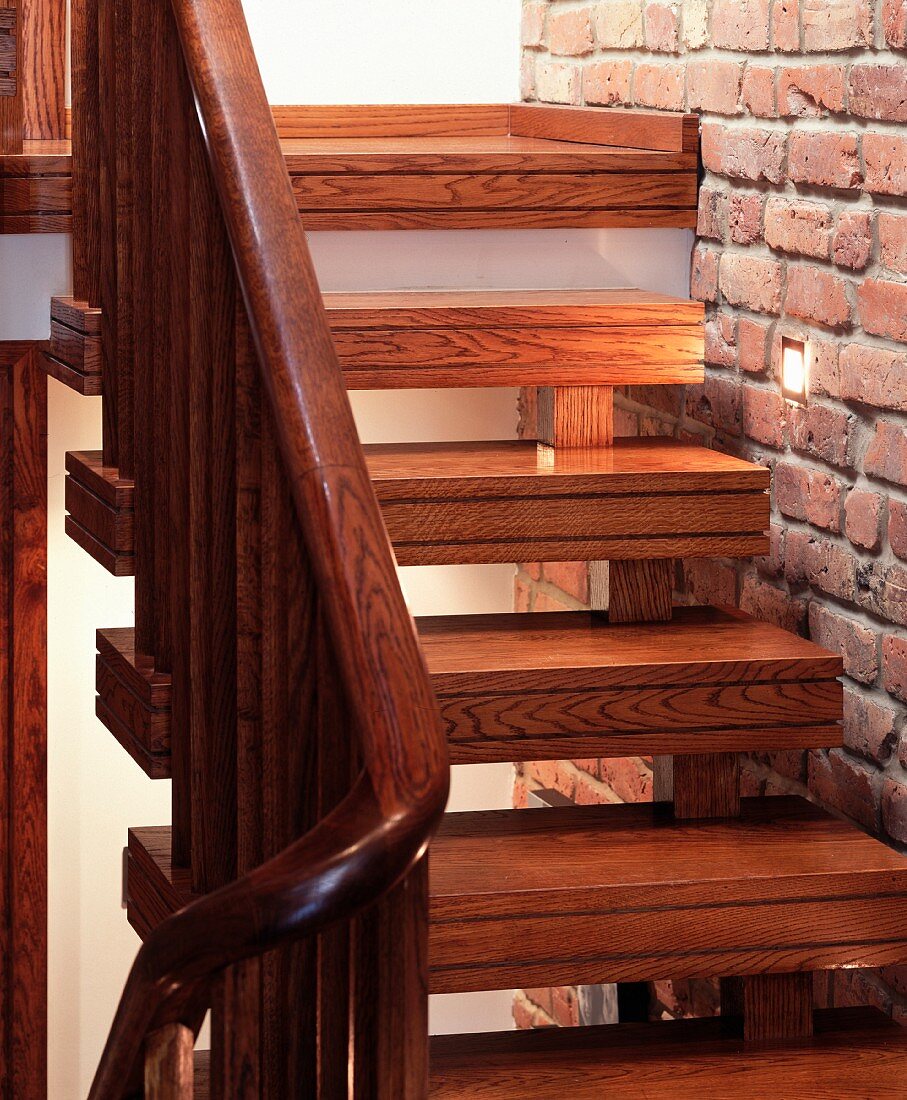 Wooden living room stairs ornamented with double grooves next to an exposed brick wall with recessed spotlights