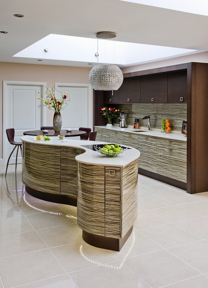 Designer kitchen with curved kitchen island in front of fitted kitchen and suspended ceiling with cut-out section