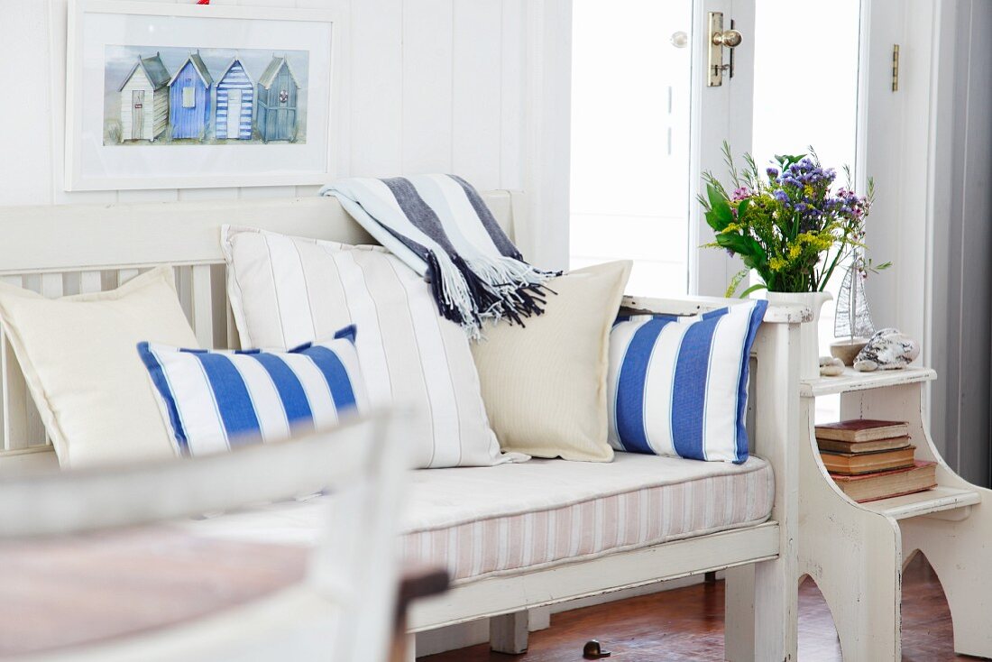 White painted bench with cushions and striped upholstery next to glass door