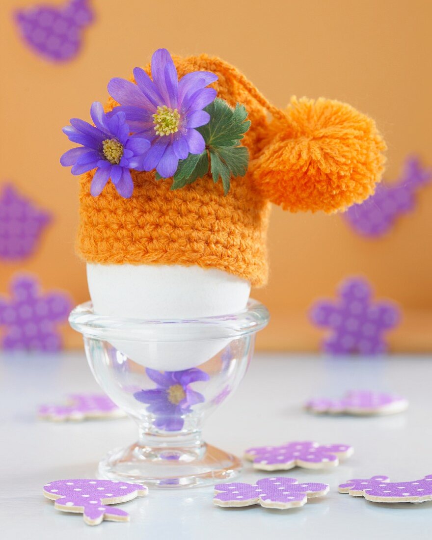 An egg in an egg cup with a crocheted egg cosy decorated with flowers