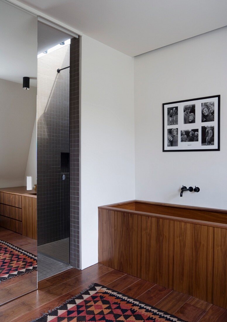 Wooden bathtub next to shower partition with mirrored sliding door