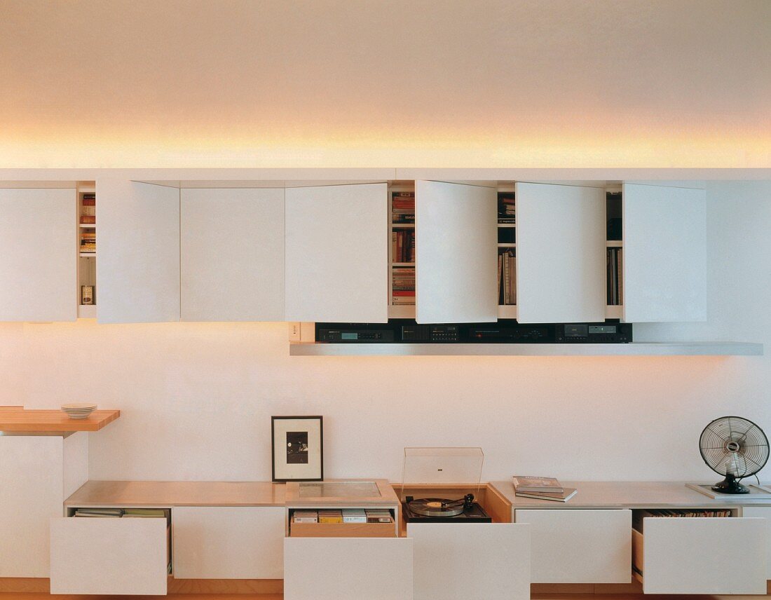 Modern, white wall-mounted cupboards and low storage units with opened doors and drawers