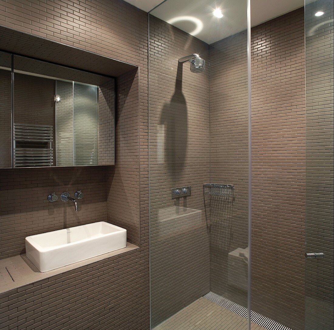 Designer bathroom with dark brown tiled walls and glass partition wall for floor-level shower