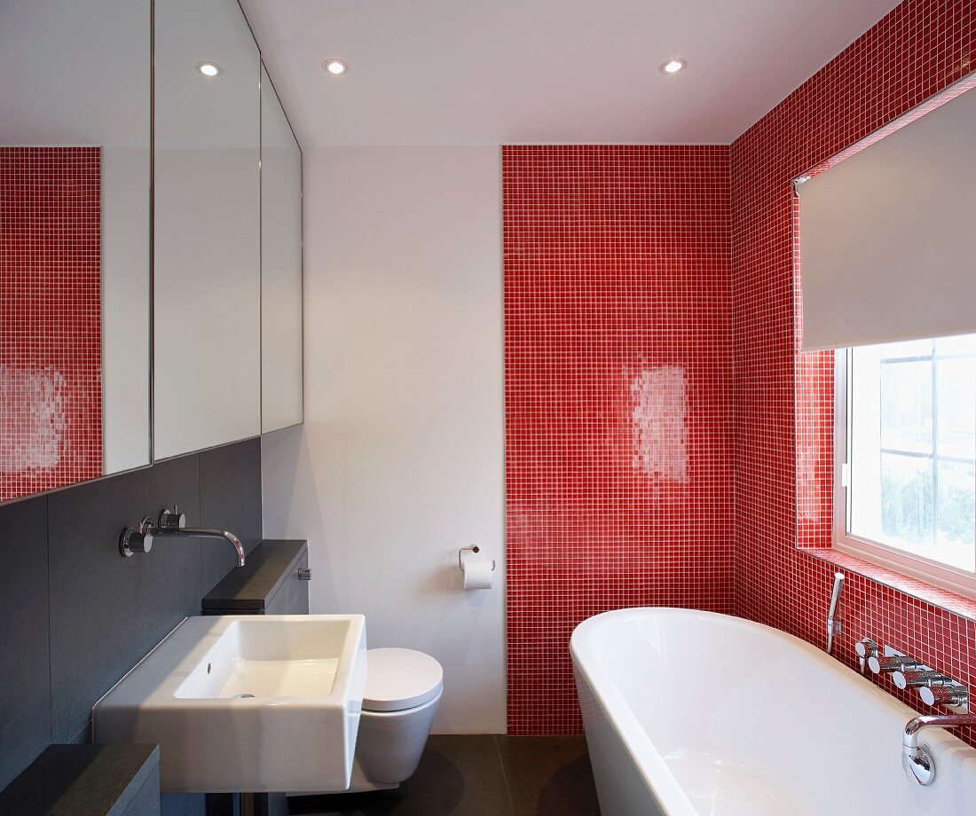 Modernes Bad mit Badewanne vor roten Mosaikfliesen und Waschbecken unter Spiegelschrank