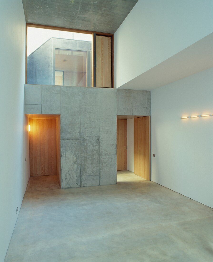 Empty foyer with large transom window and open concrete doorways leading to wooden doors