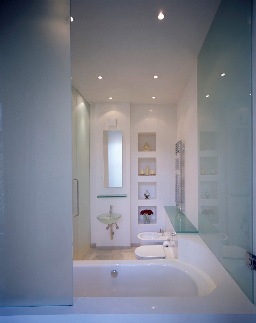 Bathtub with half-open glass partition and view into modern bathroom