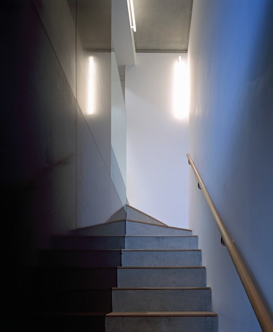 Schmaler Treppenaufgang mit schwarzen Steinfliesen an Wand und Handlauf aus Holz