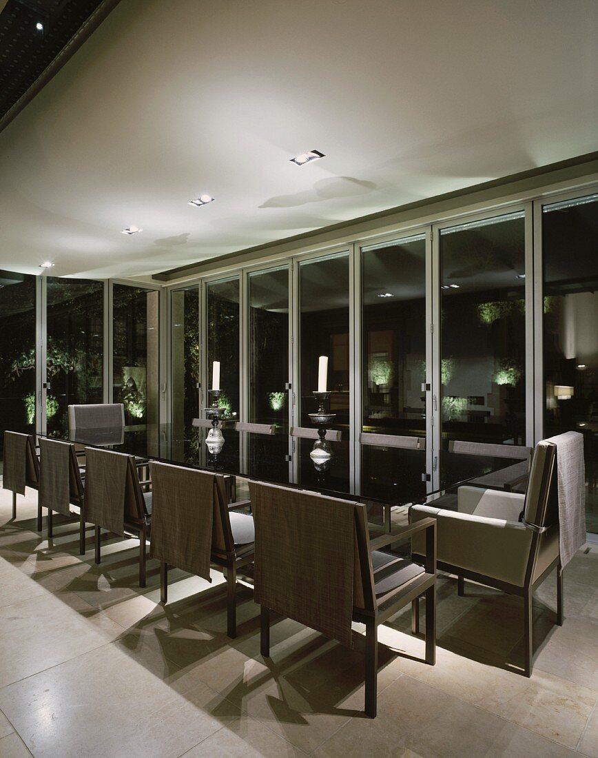 Moderner Esstisch mit eleganten Stühlen im verglasten Wohnraum mit Nachtstimmung