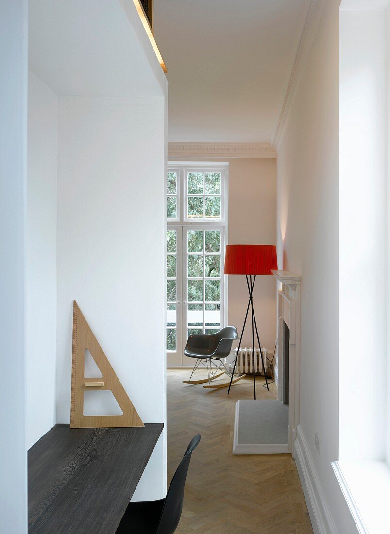 Moderne Arbeitsecke in Nische und Blick durch schmalen Durchgang auf Stehlampe im minimalistischen Ambiente