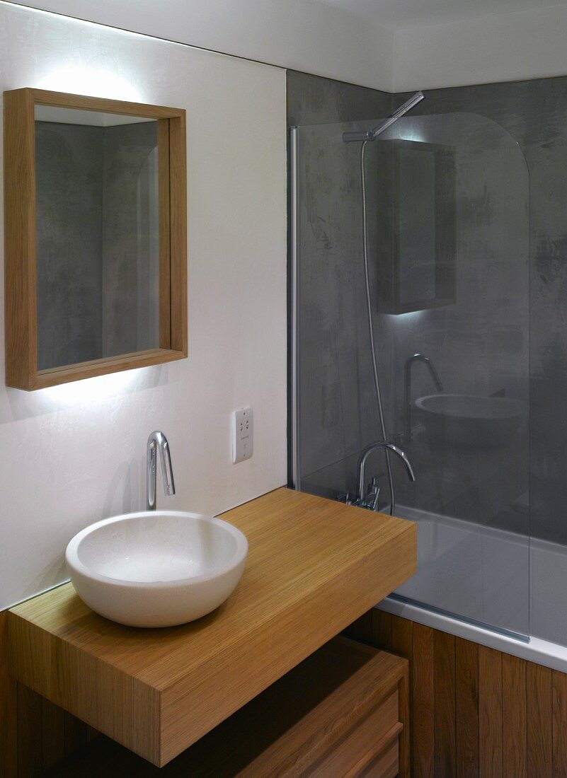 Moderner Waschtisch mit weisser Keramikschüssel auf Holzpodest und Badewanne mit Glastrennwand