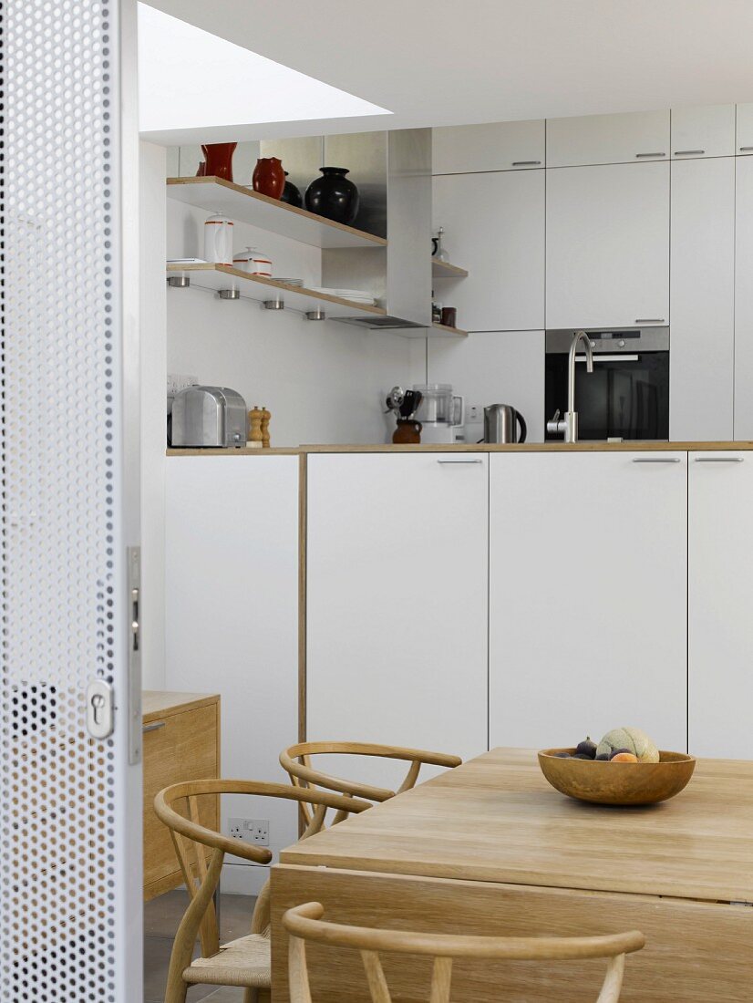 Open sliding door in perforated metal with view into kitchen with classic chairs in dining area
