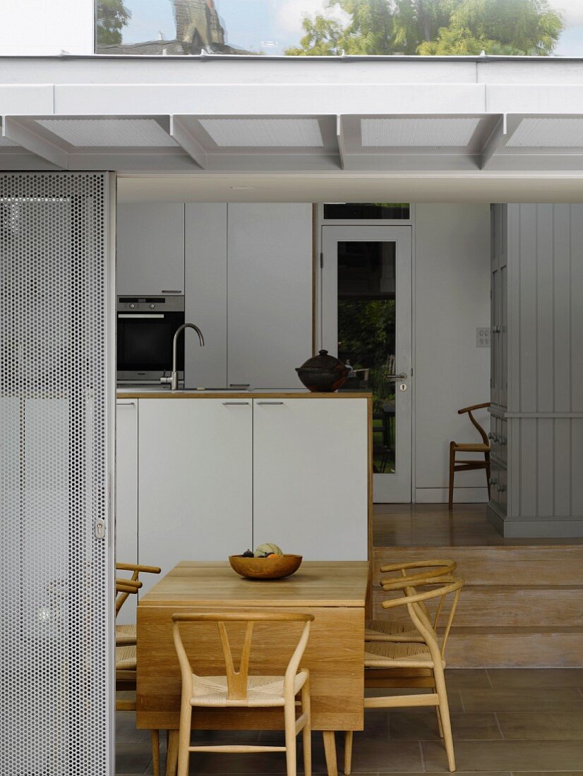 View of dining area with classic chairs and a modern kitchen through open sliding terrace door