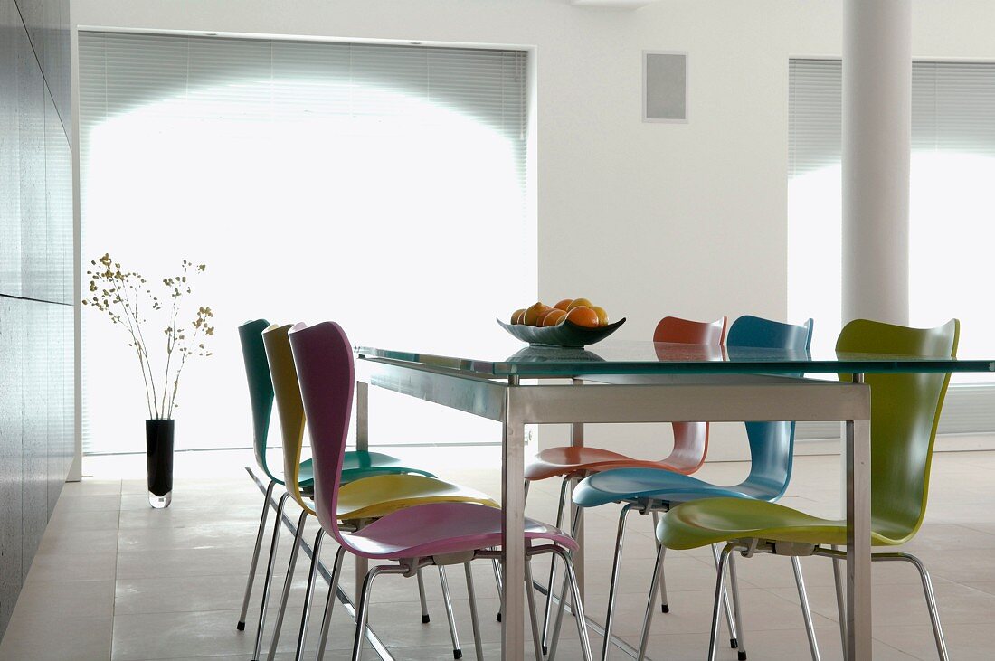 Essplatz im weissen Loftraum - farbige 50er Jahre Holzstühle an Esstisch mit Glasplatte und Stahlrahmengestell