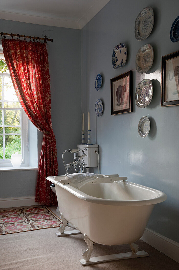 Freestanding bathtub in blue bathroom with red curtains and wall plates