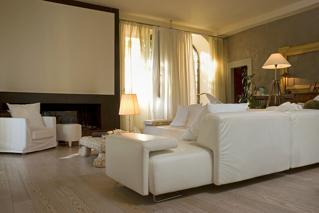 Wohnzimmer mit Kamin, weißer Ledercouch und hellem Holzboden