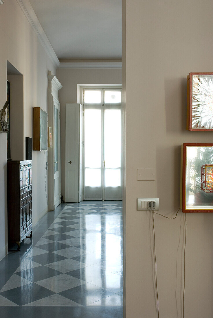 Long hallway with chequerboard pattern tiles and wall lighting