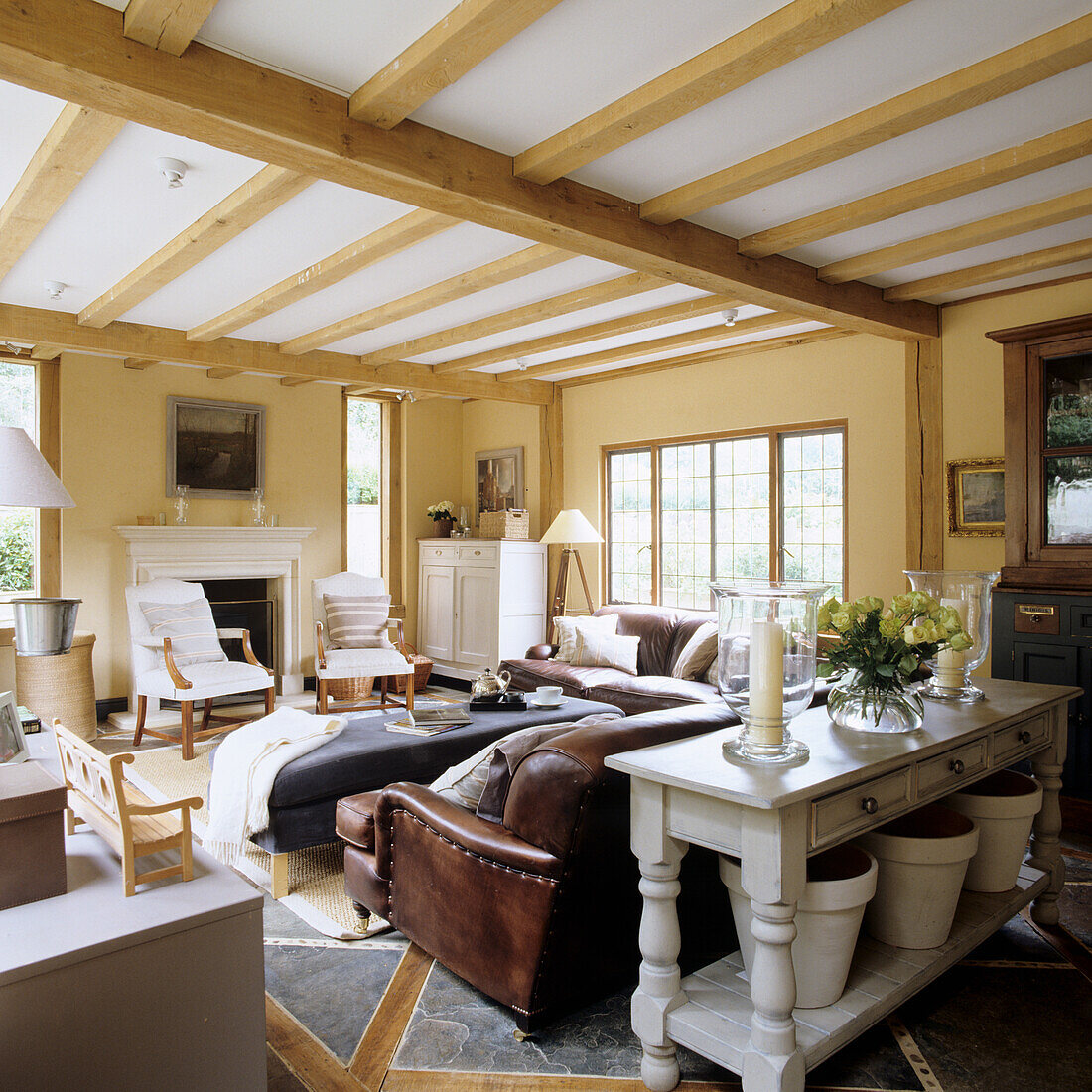 Living room with wooden beamed ceiling and fireplace, leather sofa and leather armchair