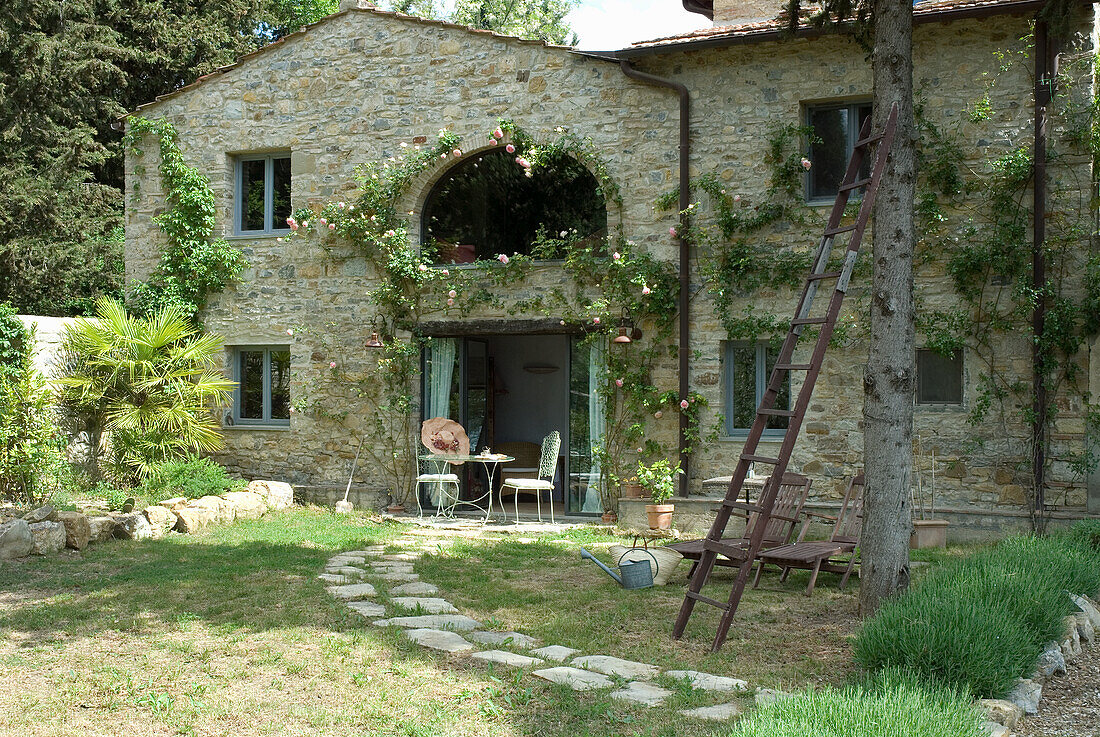 Steinhaus mit Rosengewächs und Sitzbereich im ländlichen Garten