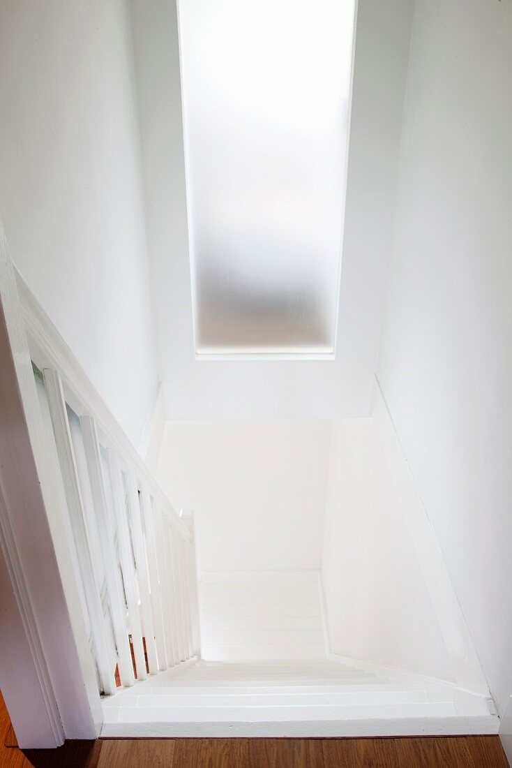 Blick von oben auf den Abgang einer weissen Landhaustreppe mit Milchglasfenster zum gegenüberliegenden Raum