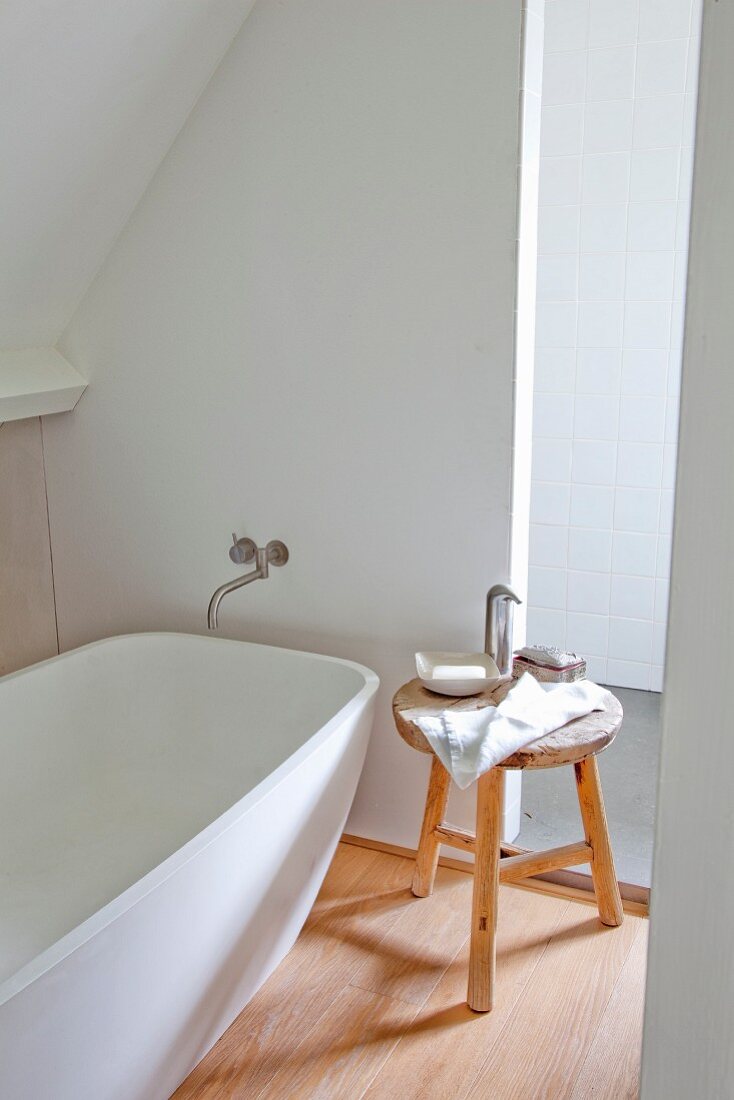 Soap dish and towel on wooden stool next to free-standing, designer bathtub in converted attic