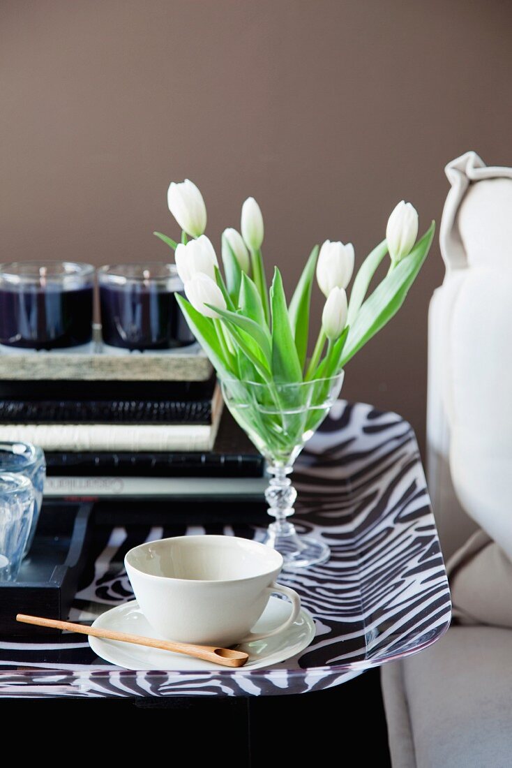 White tulips in glass and coffee cup on zebra-patterned tray