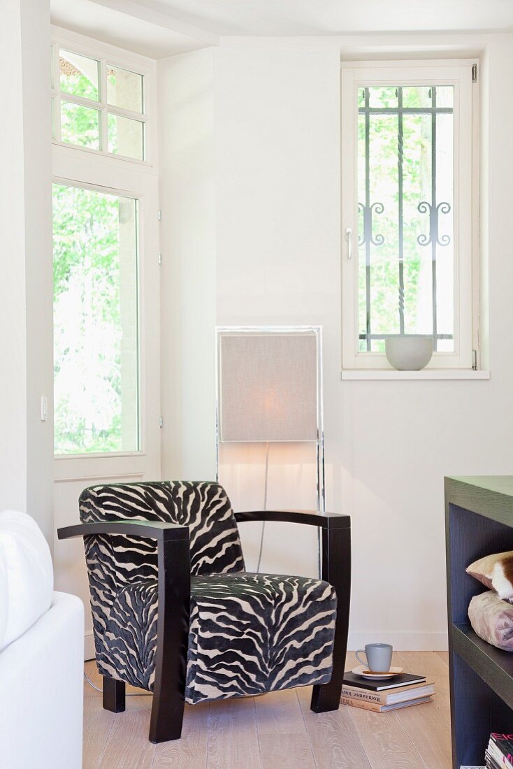 Retro armchair with zebra-patterned upholstery in front of modern standard lamp in corner