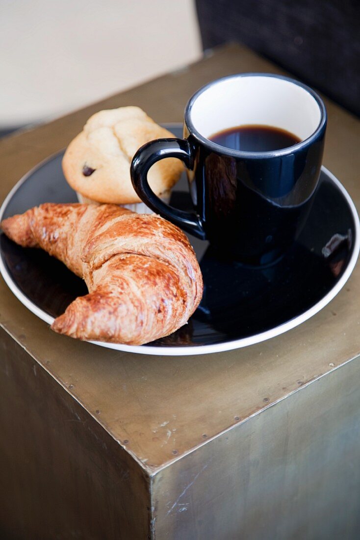 Cup of coffee, croissant and muffin on black plate
