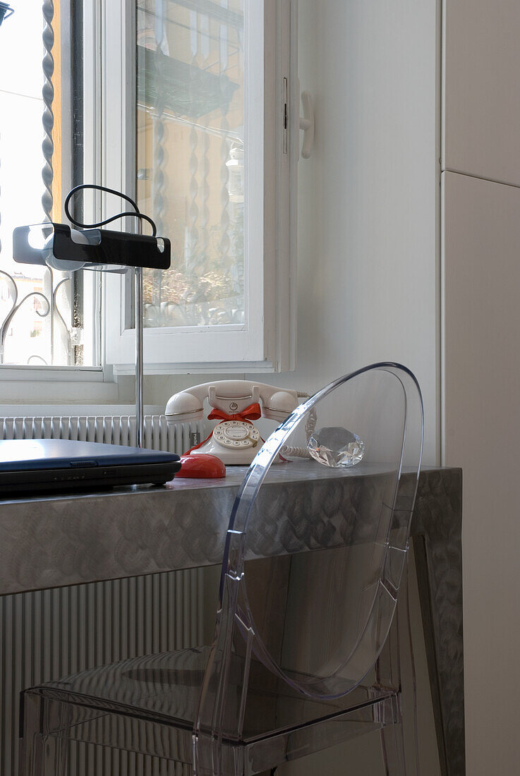 Transparent acrylic chair and desk with retro telephone in front of window