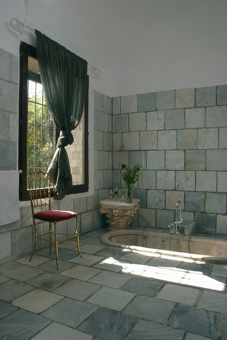 Reclaimed stone tiles and sunken marble bathtub in bathroom