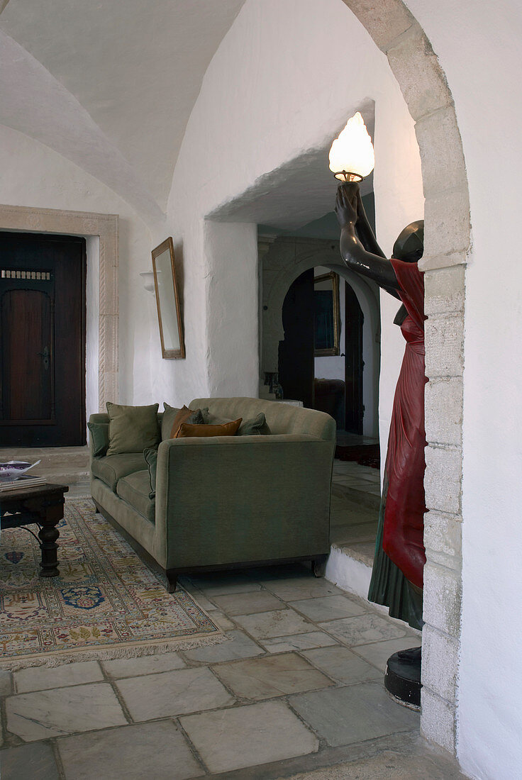 Sofa und Skulptur im Wohnzimmer mit Gewölbedecke, im Vordergrund lebensgroße Frauenstatue mit Lampe