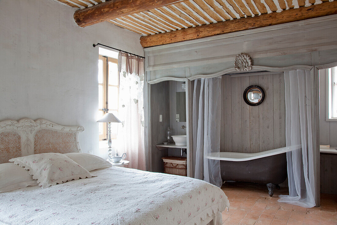 Country-style bedroom with free-standing bathtub and wooden beamed ceiling