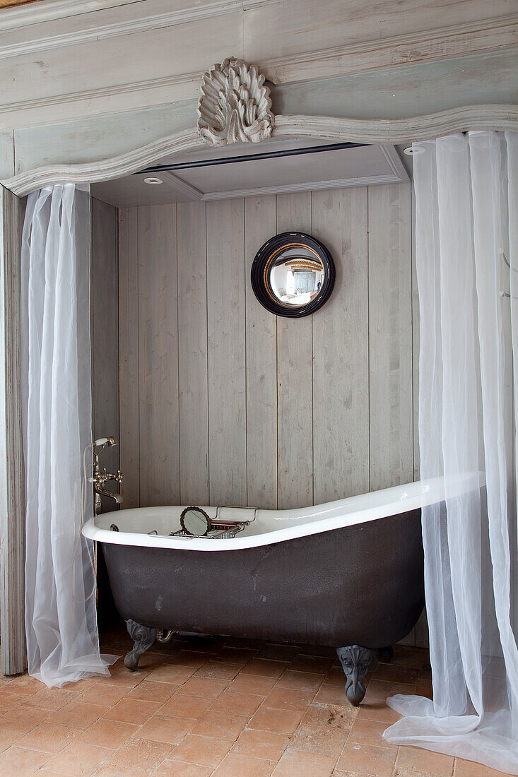 Freestanding vintage bathtub with lion feet surrounded by white curtains