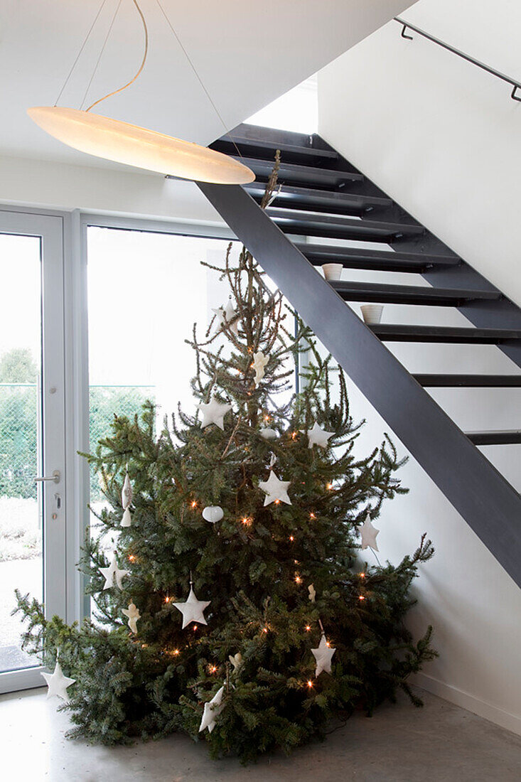 Christmas tree with fairy lights and white stars next to modern staircase