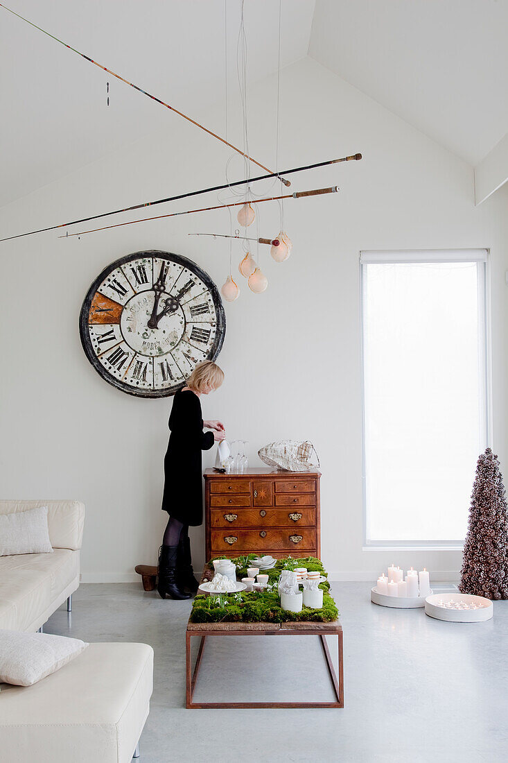 Person creates Christmas table decorations in the bright living room with a large wall clock