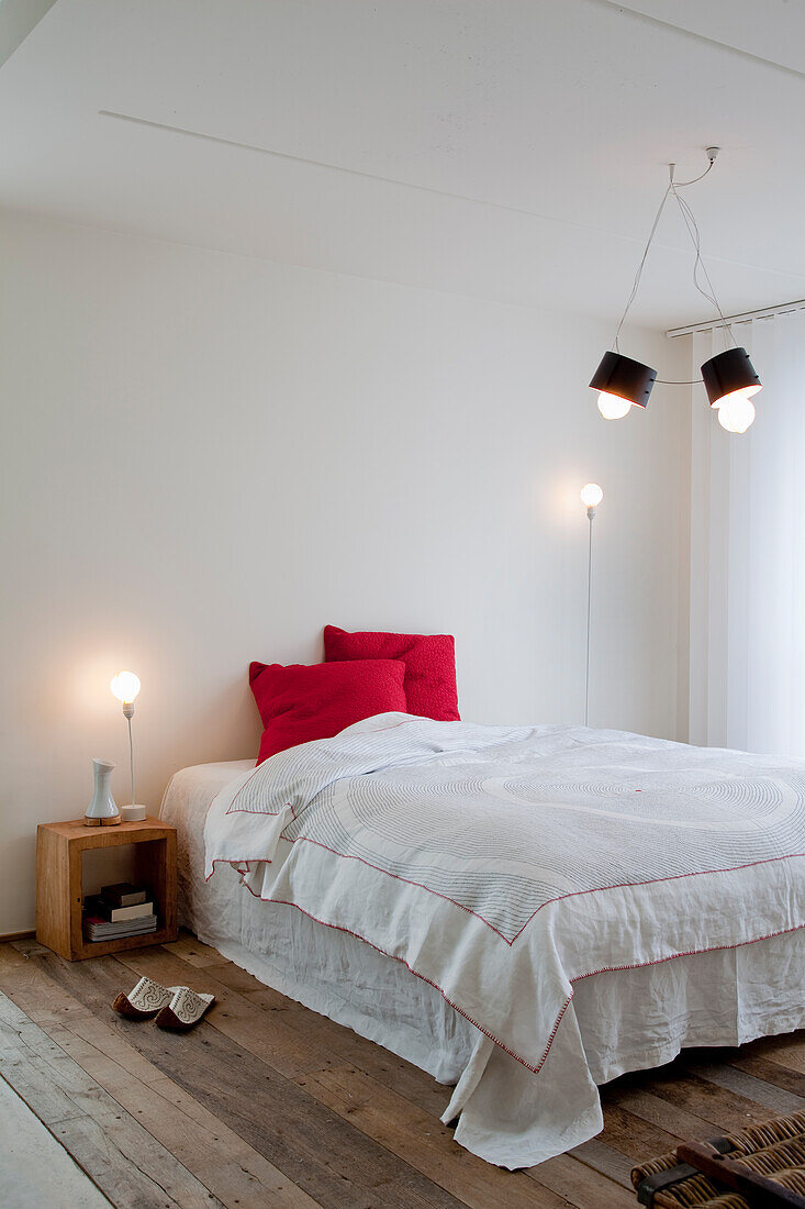 Minimalist bedroom with wooden floorboards and red accent cushions