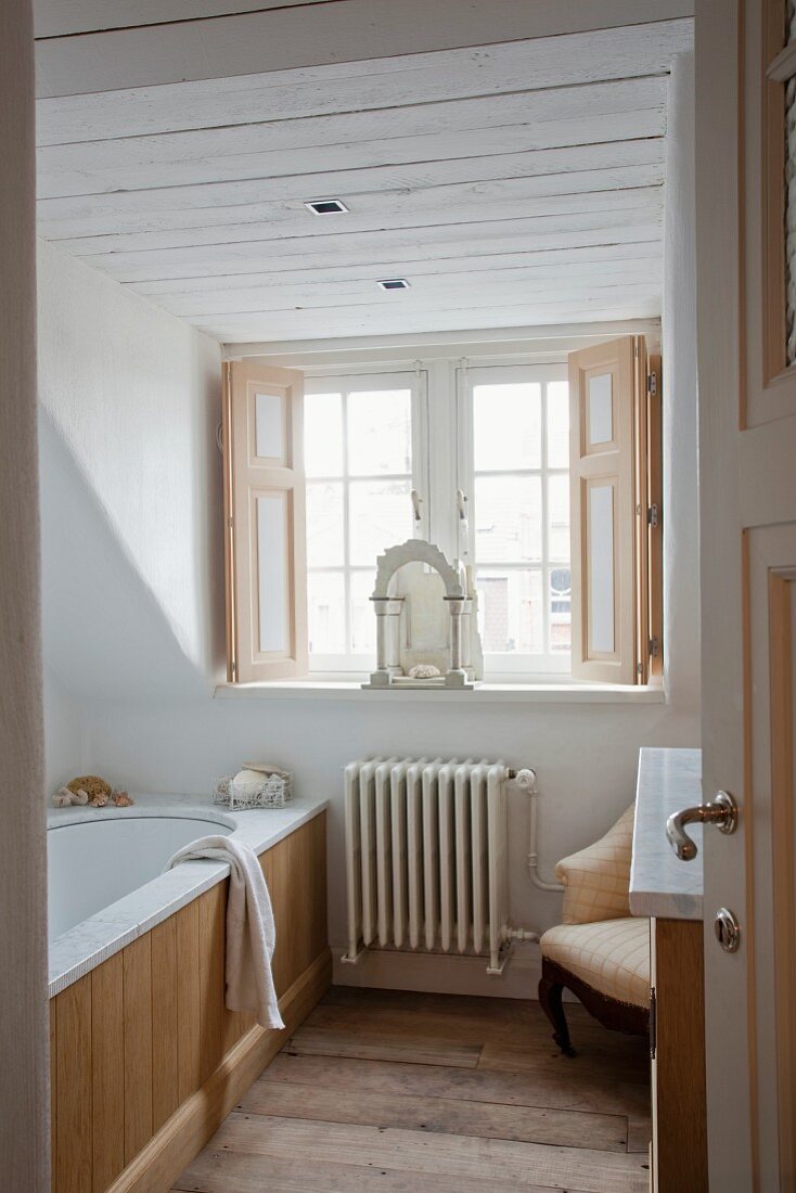 View through open door into bathroom with bathtub next to dormer window