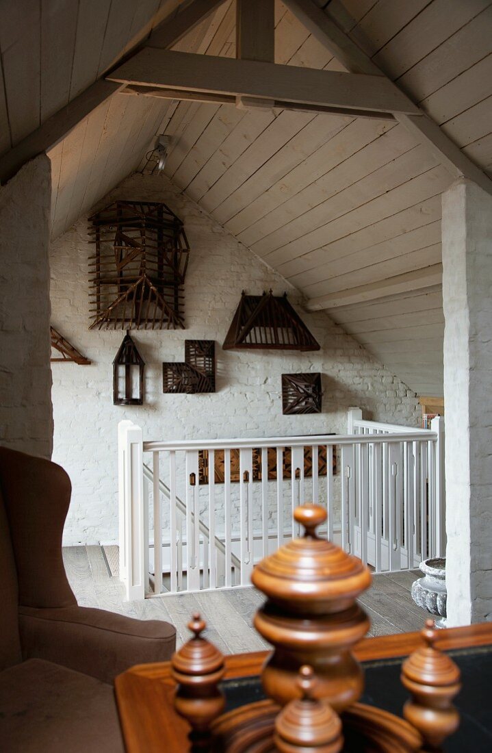 Open-plan attic room with wooden ceiling and wooden models hung on wall at head of stairs