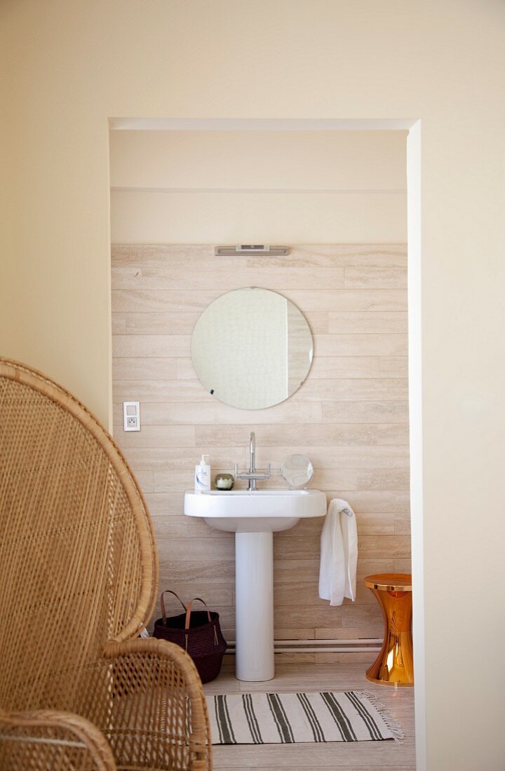 Wicker peacock chair in front of doorway leading to ensuite bathroom - shiny, gold vintage stool next to traditional pedestal sink