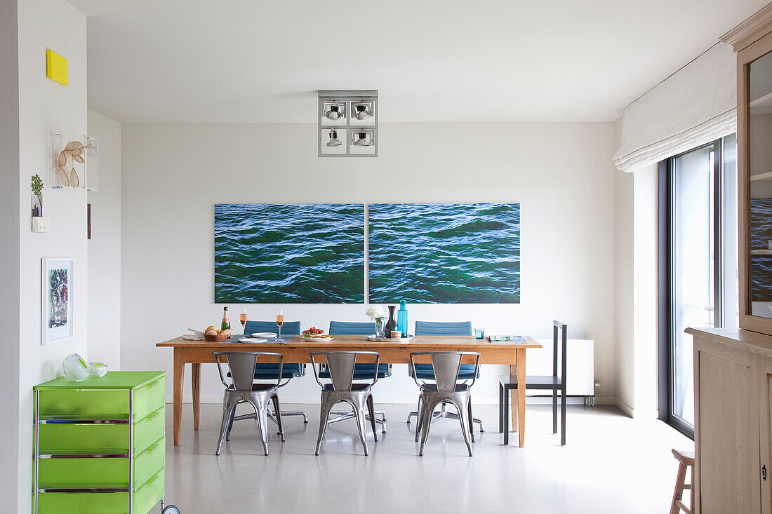 Brightly furnished dining room with large seascape on the wall