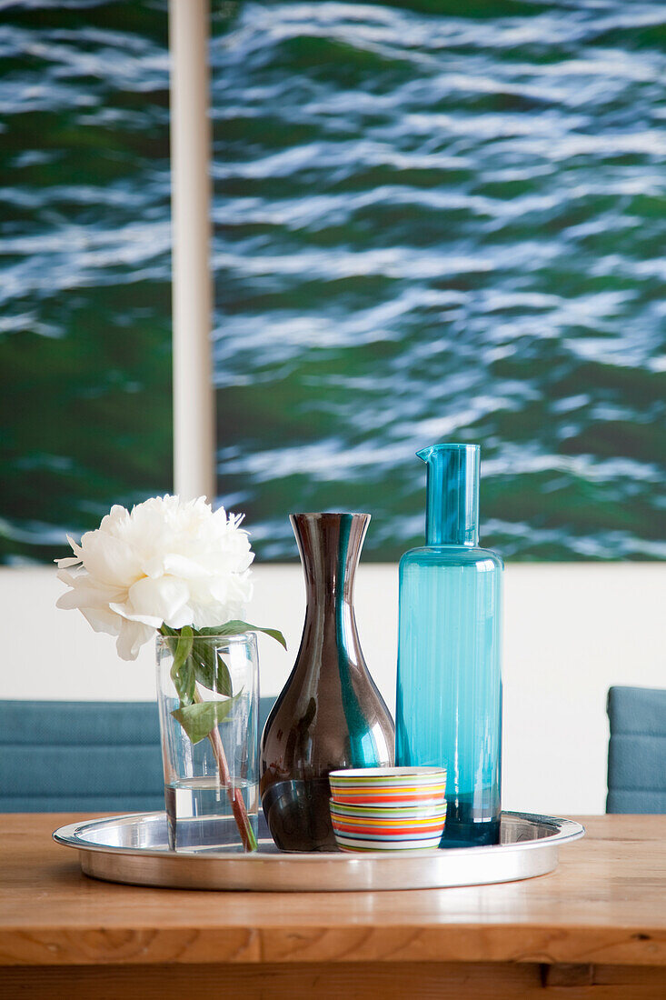 White peony in glass vase on tray next to colourful bowls and vases