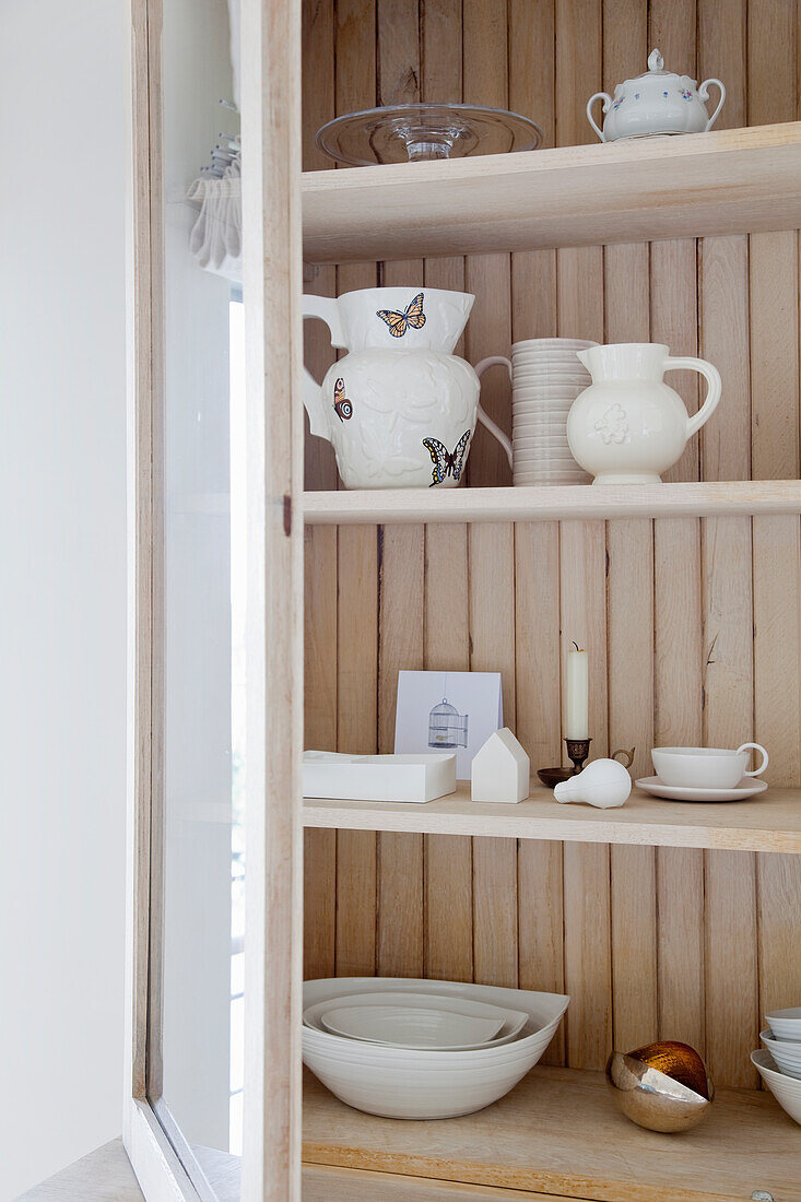 Light wood display cabinet with white crockery and decorative elements