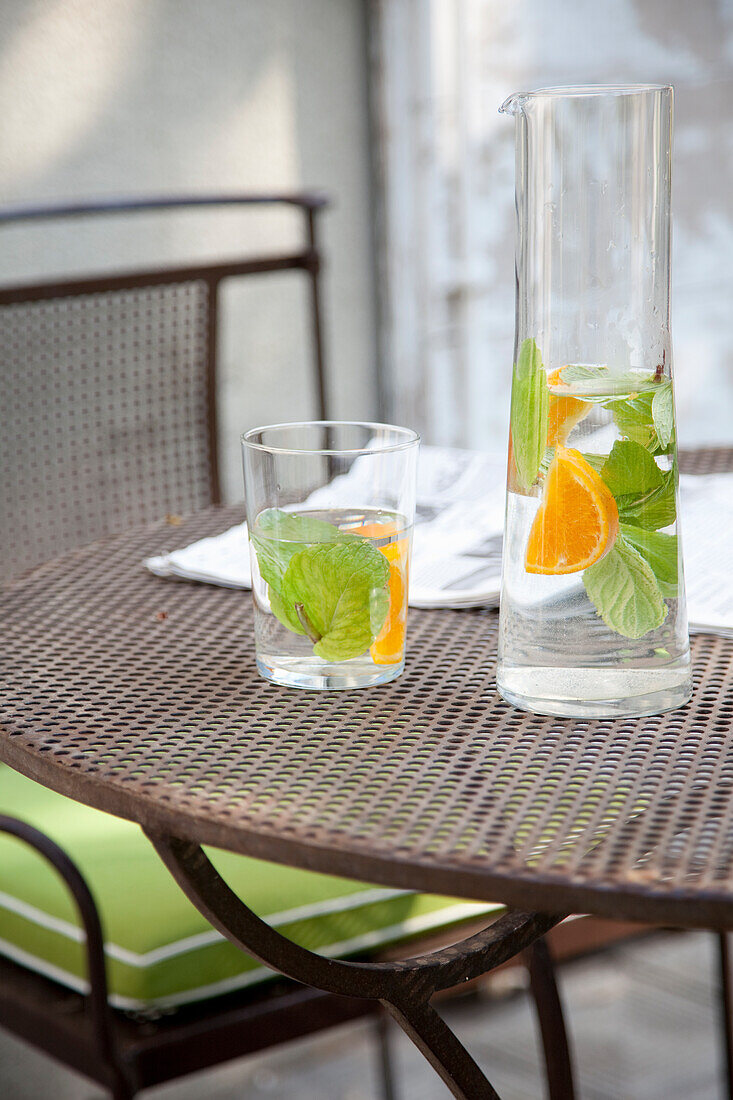 Krug mit Wasser, Minze und Orangenscheiben auf einem Gartentisch