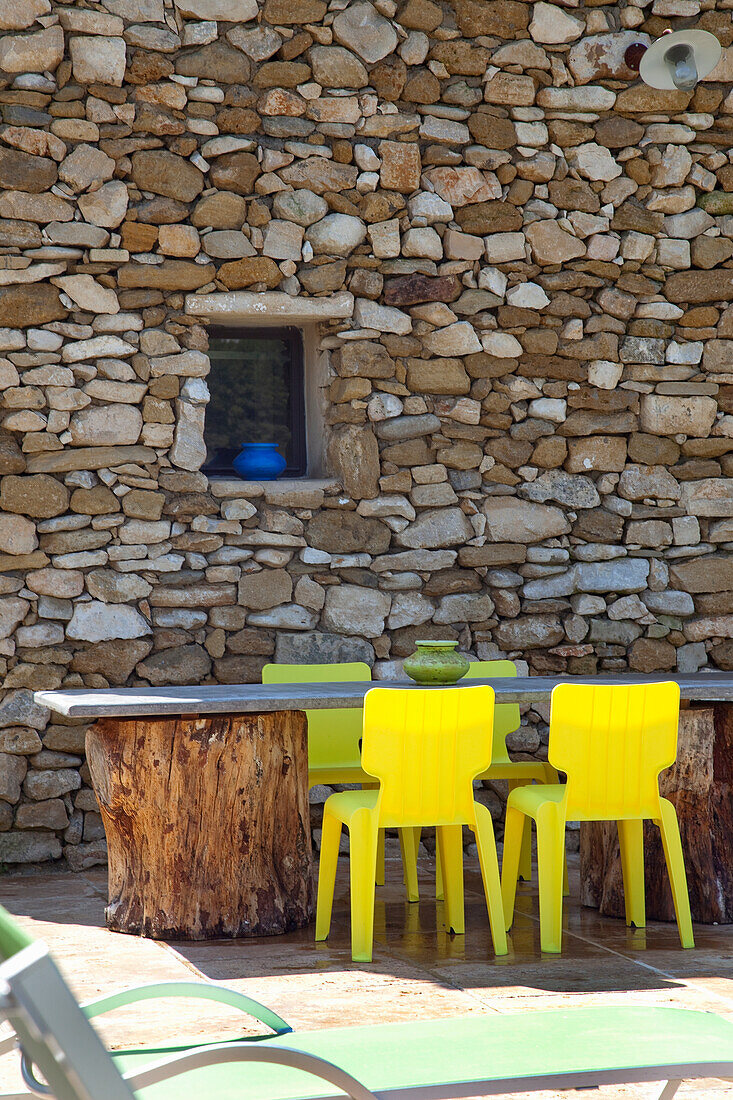 Stone table with yellow chairs in front of rustic stone wall in outdoor area